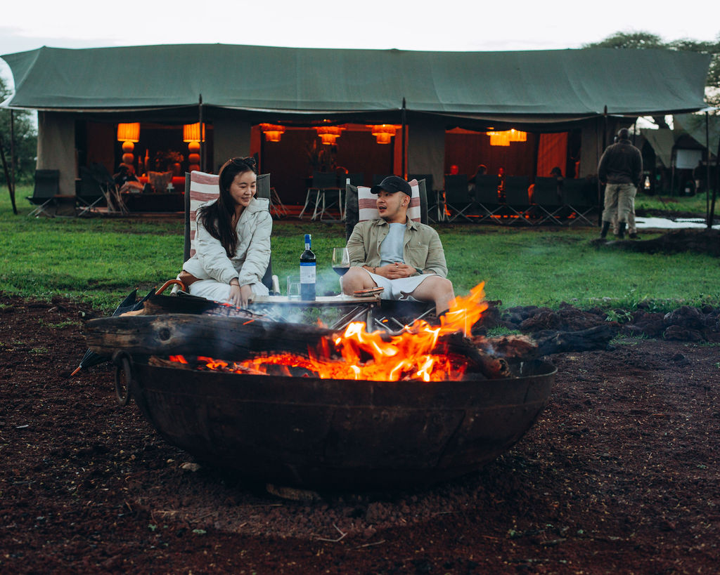 Campfire burning in front of a row of lit safari tents at nightfall