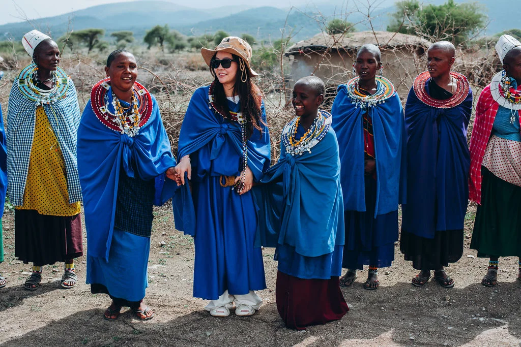 Guest standing with Maasai women in blue shukas and beaded collars