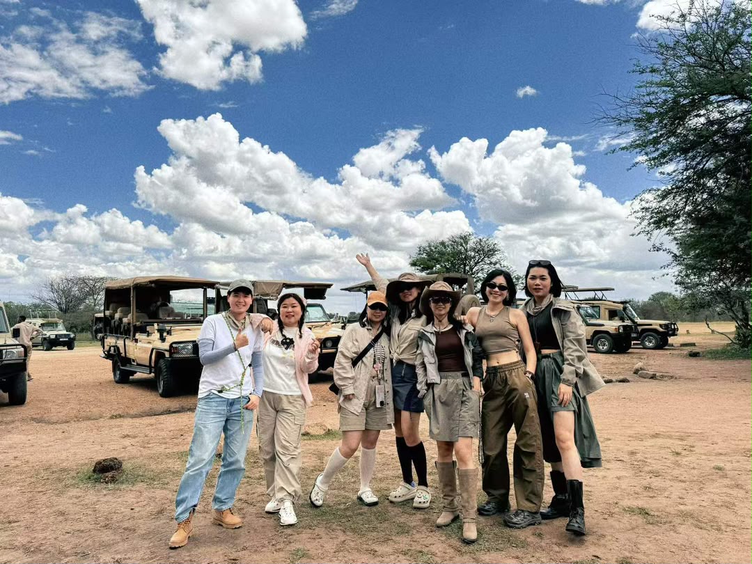 Group of safari guests photographed beside their vehicles on the plains