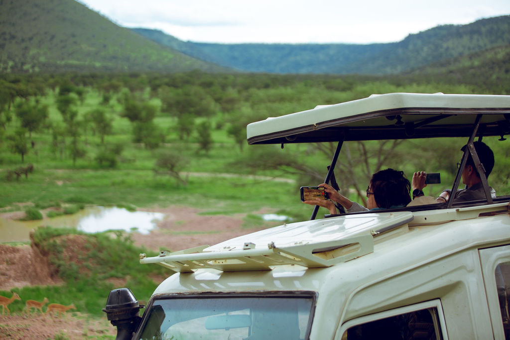 Guests photographing from the safari vehicle above a green valley