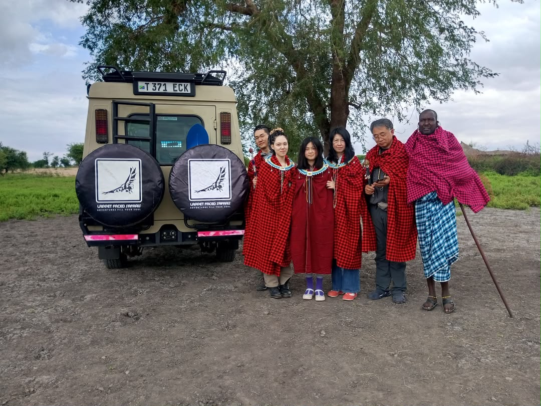 Guests with Maasai hosts in traditional dress beside a safari vehicle