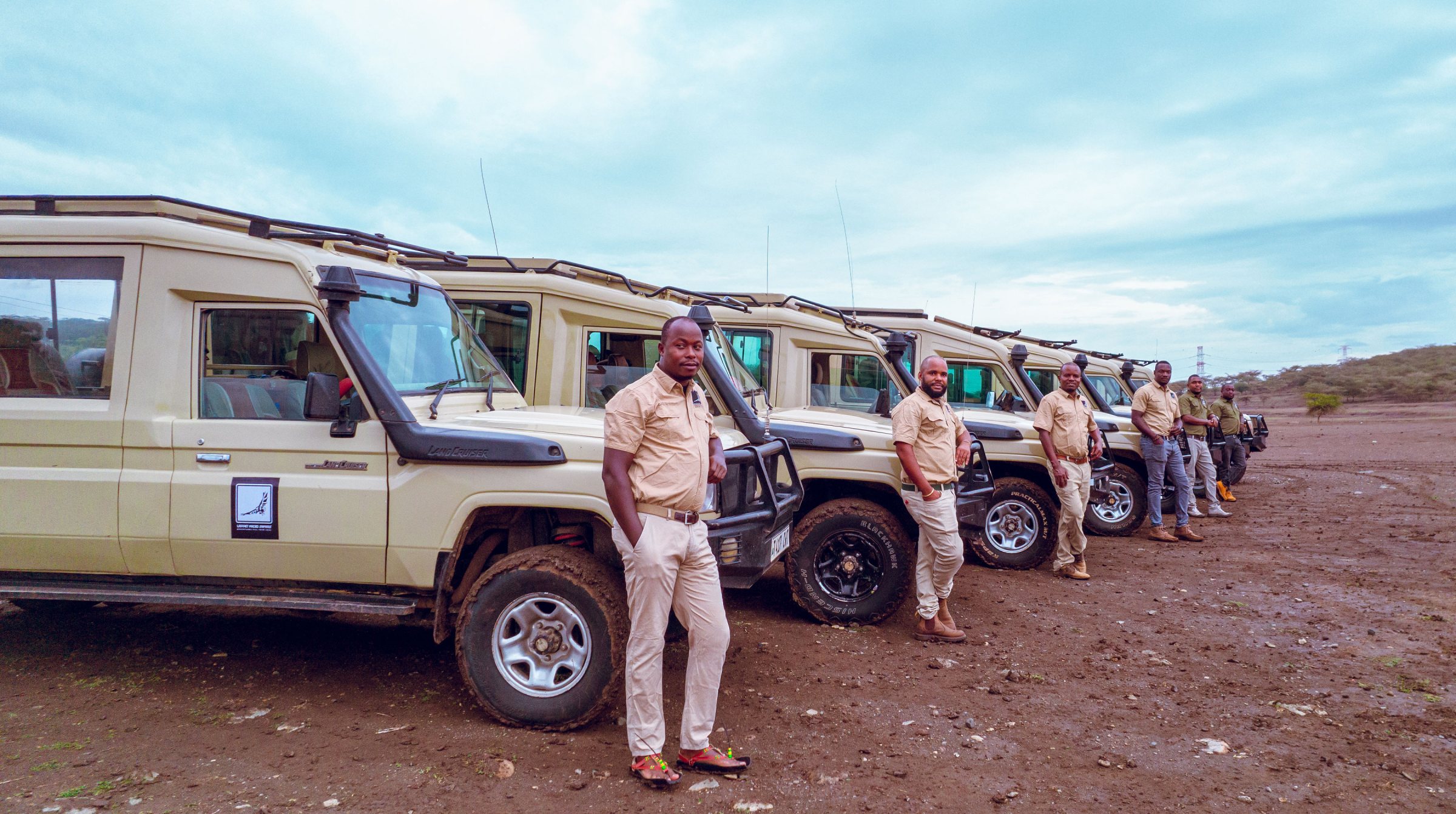 Lappet Faced Safaris guides standing beside a row of safari Land Cruisers