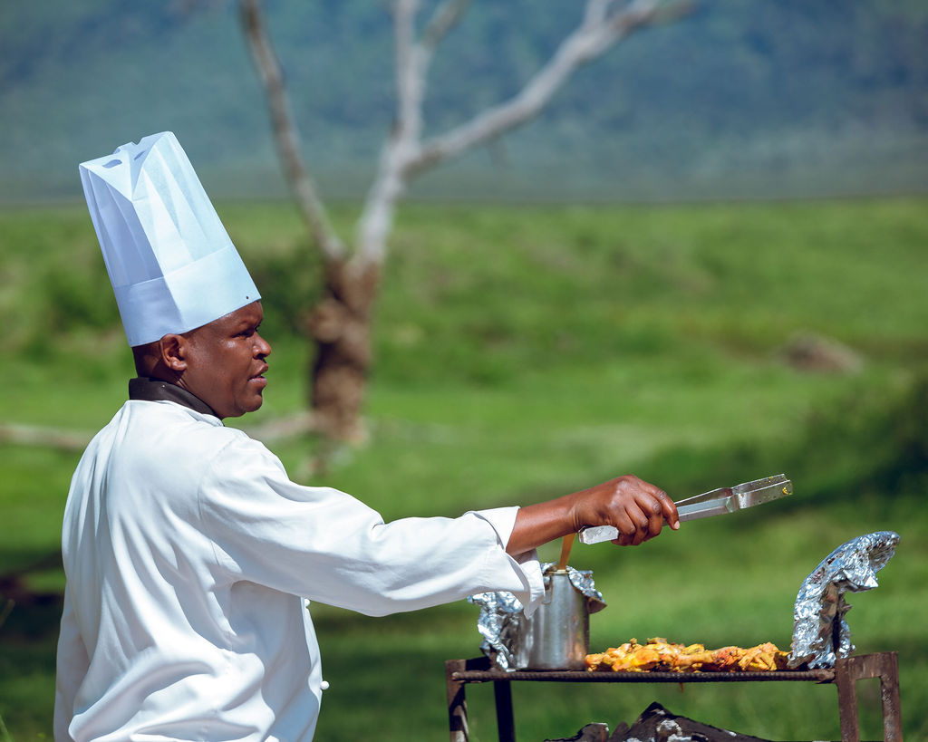 Safari chef in whites cooking over a field kitchen in the bush