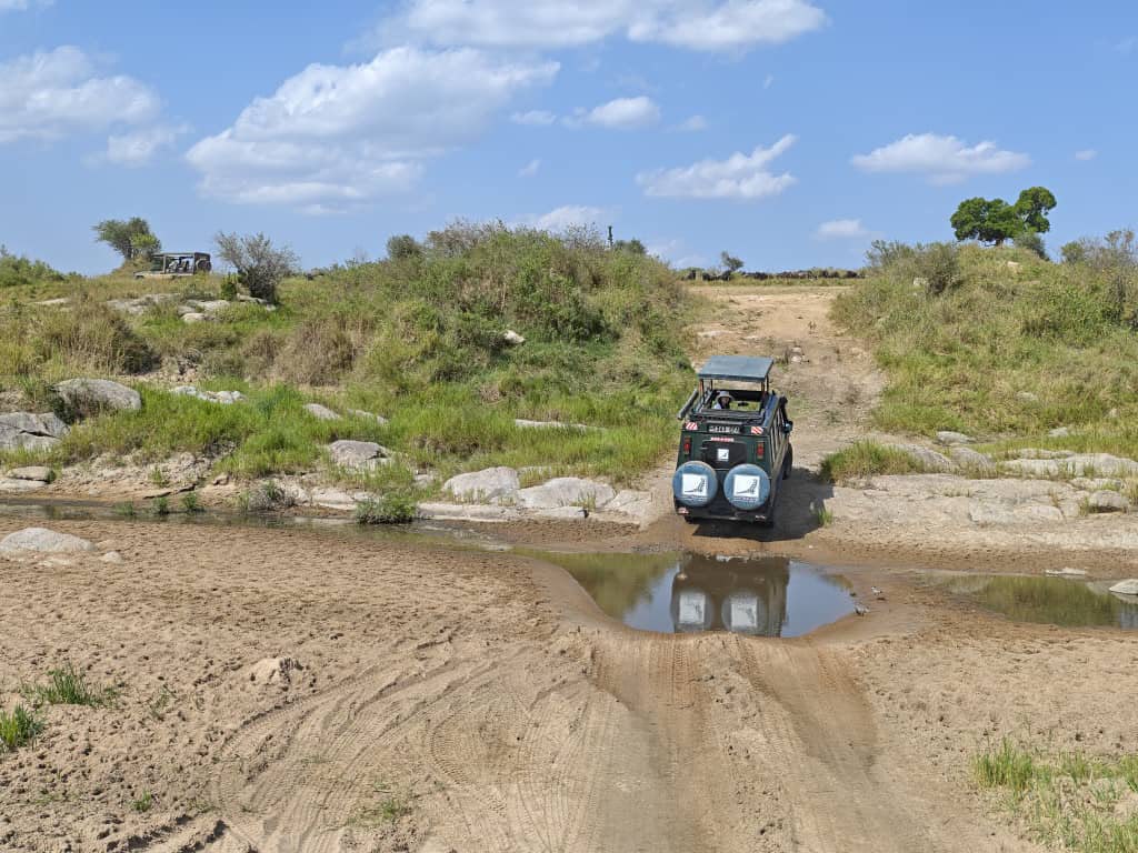 Safari vehicle crossing a shallow rocky river on a game drive